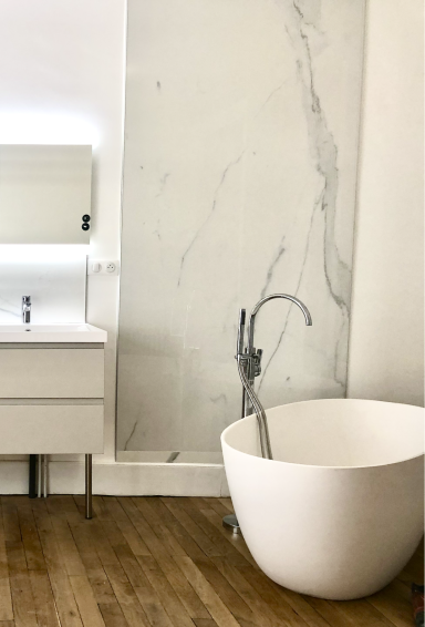 Salle de bain moderne avec baignoire îlot blanche et faïence géante.