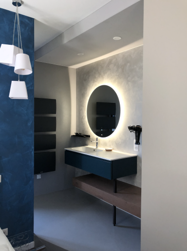 Salle de bain moderne avec miroir circulaire rétro-éclairé et meuble sous vasque en bois.