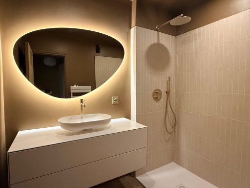 Salle de bain moderne avec miroir lumineux, lavabo et douche séparée.