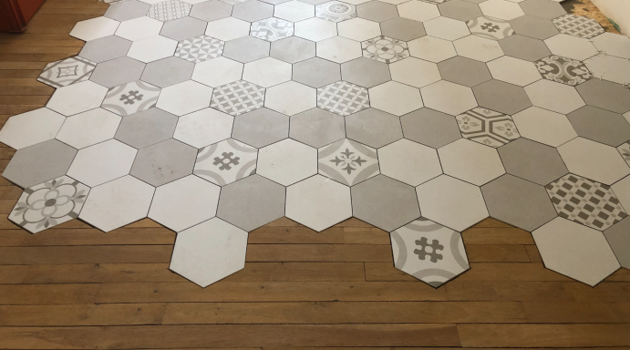 Carrelage hexagonal carreaux de ciment insérré sur un sol en bois, motifs variés.