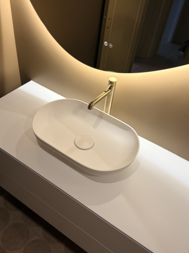 Lavabo ovale blanc avec robinet doré sur un meuble au design moderne.