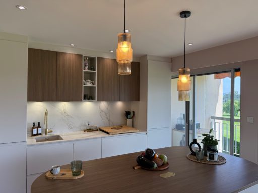 Cuisine moderne avec des plans de travail clairs, éclairage suspendu et fruits sur la table.