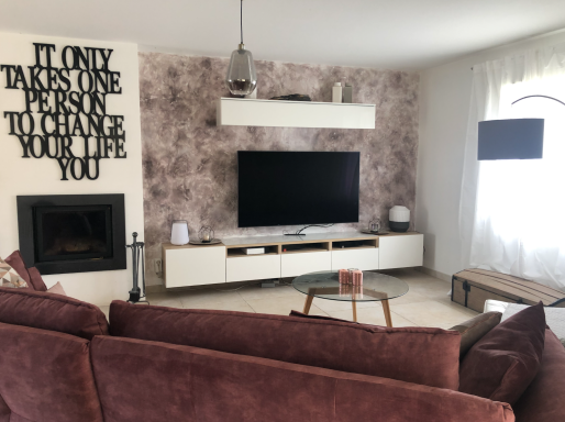 Salon moderne avec un canapé prune, télévision murale et décoration cheminée.