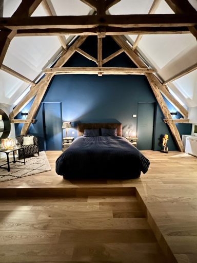 Chambre mansardée avec lit, murs bleu foncé et poutres apparentes.