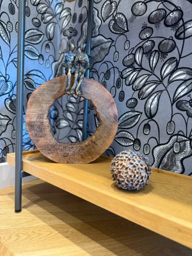 Objet décoratif en bois rond avec une boule ornée de motifs, sur une étagère en bois.