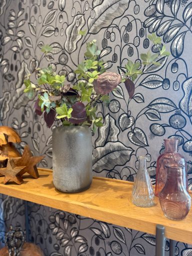 Vase avec des branches vertes et pourpres sur une étagère en bois, décor mural floral.