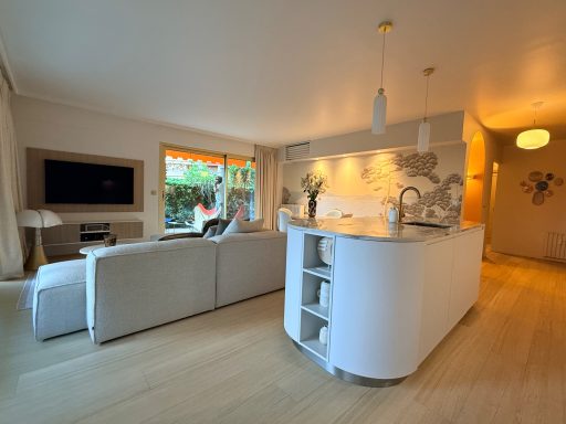 3 pièces le Wiosna, Cannes Salon moderne avec un coin cuisine, canapés clairs et fenêtre ouverte sur l'extérieur.